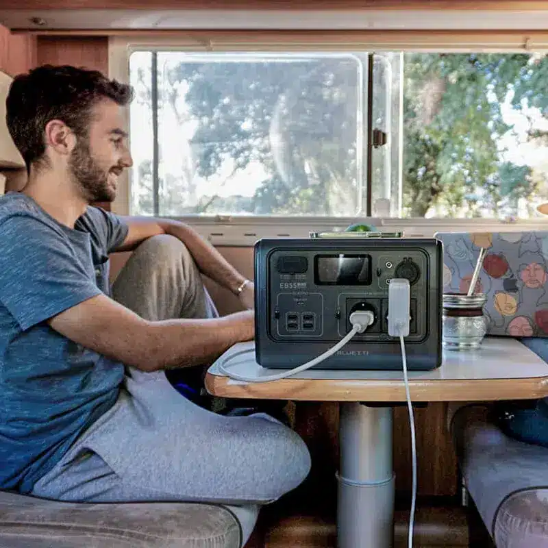 Un voyageur est assis dans son van et utilise sa station énergie portable EB55 Bluetti, pour brancher ses appareils électroniques.
